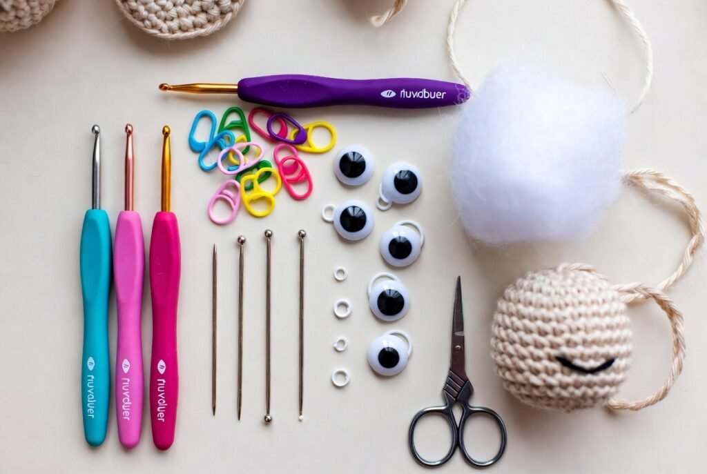 Crochet tools for amigurumi including small crochet hooks, stitch markers, tapestry needles, safety eyes, and stuffing displayed with a finished amigurumi toy.